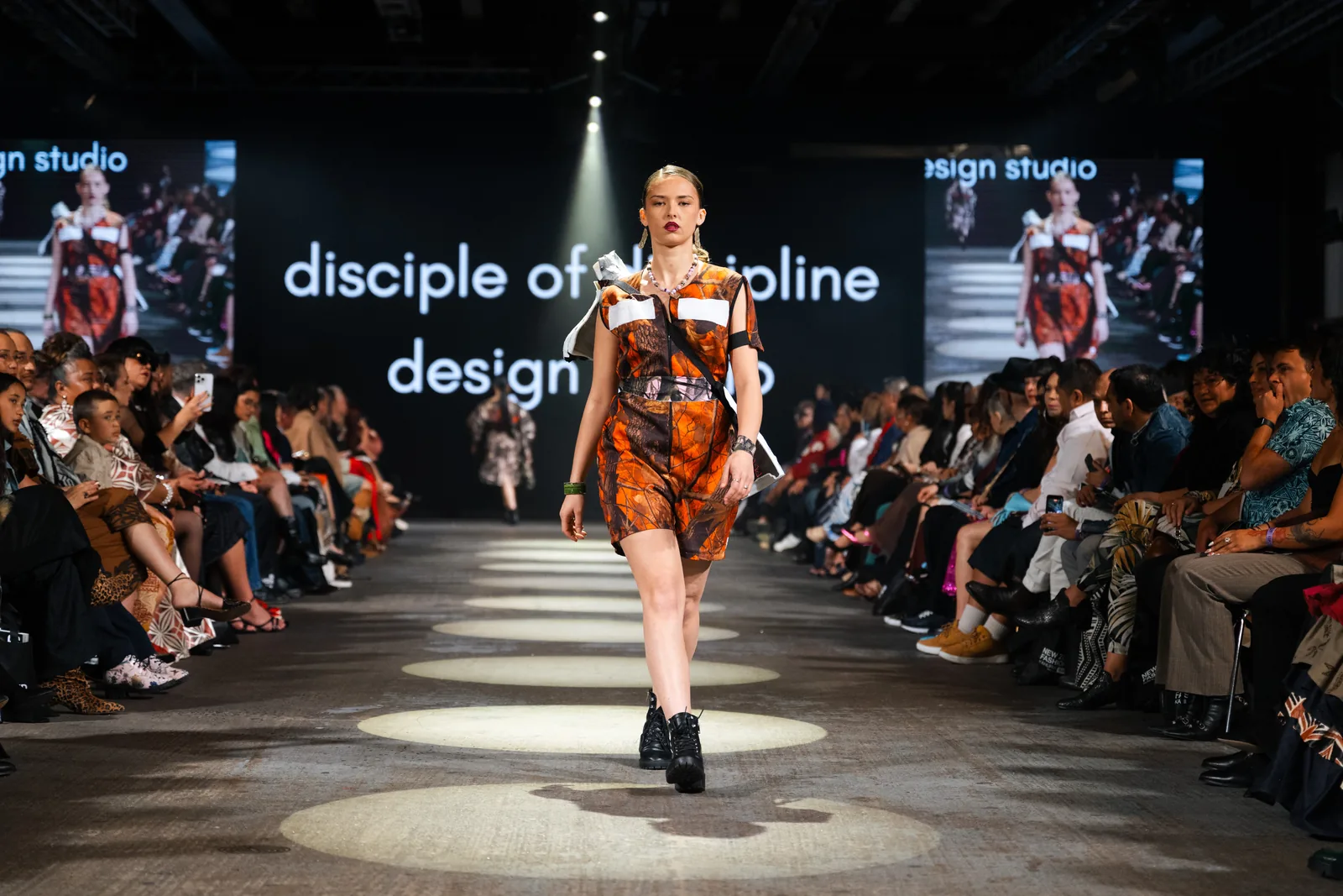 An orange print playsuit with white panels and a black harness on the runway