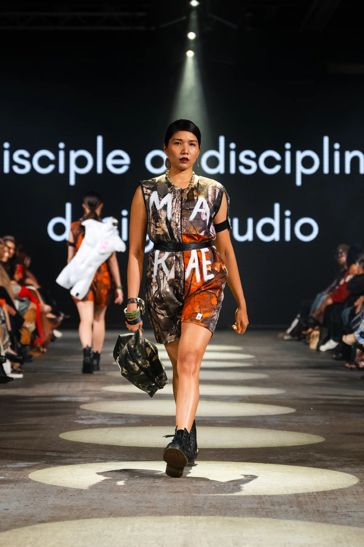 A print dress with white lettering and a black bag on the runway