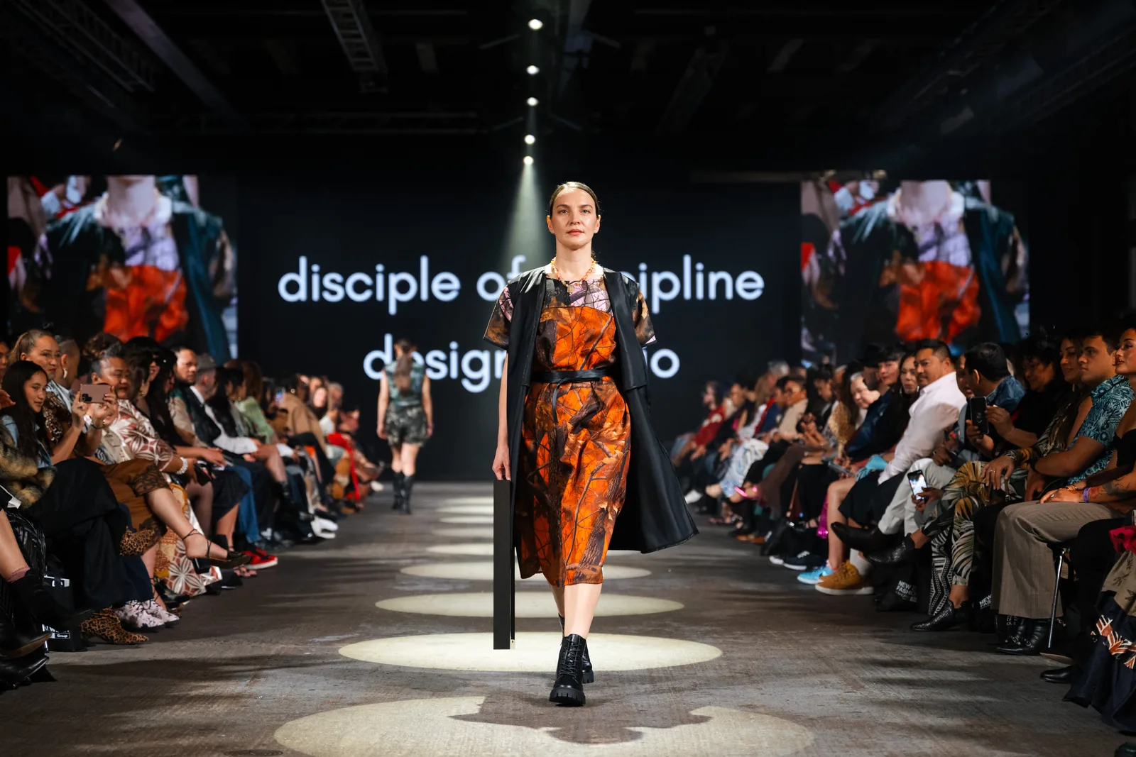 An orange print dress under a long black coat on the runway